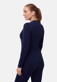 Maglietta a maniche lunghe blu navy con design aderente e colletto a girocollo. Caratterizzata da una texture liscia e cuciture piatte per il comfort. Abbinata a leggings coordinati.