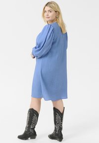 Vestido azul texturizado con mangas largas abullonadas, a la altura de la rodilla. Se lleva con botas de cowboy negras con diseños plateados bordados.