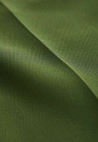 Maslinasto zeleni materijal s glatkom, blago teksturiranom površinom, prikazuje nježne nabore i valove. Svjetlost se suptilno odbija od materijala.