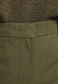 Olijfgroene broeken van een gladde, geweven stof. Heeft een platte voorkant, gestikte tailleband en een minimalistisch ontwerp voor veelzijdig gebruik.