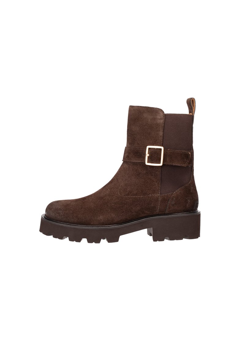 Stivale alla caviglia in suede marrone con suola spessa, pannello laterale elasticizzato e cinturino decorativo con fibbia dorata su uno sfondo bianco.