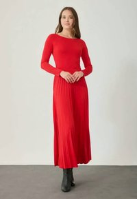 Robe longue rouge avec un corsage ajusté à manches longues et une jupe plissée. Fabriquée en tissu doux, elle présente un col rond et tombe jusqu'aux chevilles.