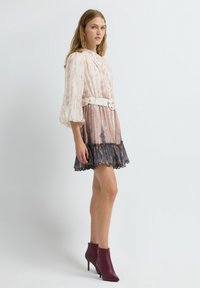 Abito leggero, tie-dye in rosa e marrone, con maniche a sbuffo, vita con cintura e orlo rifinito in pizzo. Abbinato a stivaletti alla caviglia bordeaux.