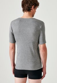 T-shirt grigio a maniche corte realizzata in tessuto morbido, design aderente e scollatura a girocollo. Indossato con pantaloni corti neri, che mostrano la vista posteriore.