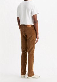 Brązowe sztruksowe spodnie o wąskim kroju, z metką z tyłu na wysokości pasa. Zestawione z prostą białą koszulką z krótkim rękawem oraz białymi trampkami.