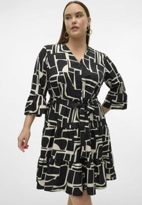 Robe noire et beige avec un motif géométrique, décolleté en V, manches trois-quarts, taille cintrée et ourlet en volants superposés. Tissu doux.