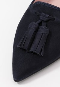 Sapata em camurça azul-marinho com bico apontado e detalhe de franjas. Textura suave e franjas decorativas na cor correspondente.