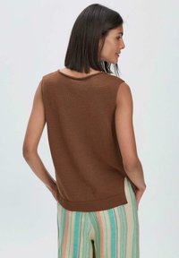 Bruine mouwloze sweater met een ronde halslijn en geribbelde zoom, gecombineerd met lichte gestreepte broeken met verticale patronen.