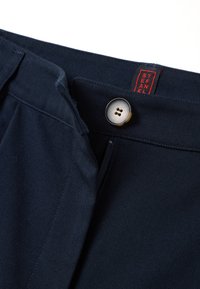 Pantalon bleu marine avec une fermeture éclair visible, une fermeture par bouton et une étiquette rouge. Il présente un tissu texturé et un design classique à plat devant.