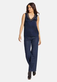 Navy satijnen mouwloos topje met een V-halslijn, versierd met zwarte kant, gecombineerd met donkerblauwe wijde jeans en zwarte hoge laarzen.