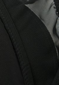 Svart mesh-tyg med fina sömnadsdetaljer som skapar en semitransparent texturerad yta, vilket framhäver tygskiktning och mönsterkontrast.