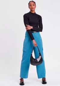 Schwarzes Langarmshirt mit strukturiertem Muster, leuchtend blaue weite Cargohose mit Seitentaschen und eine schwarze Tasche mit Krokodilprägung.