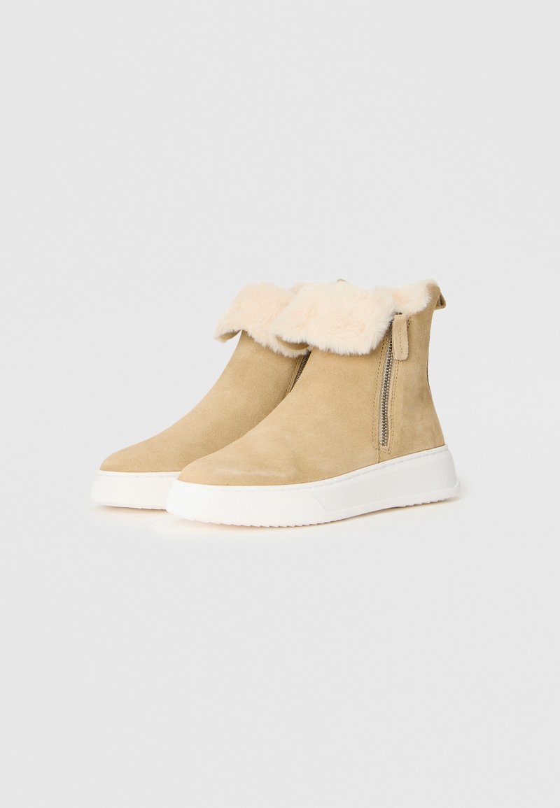 Beige mockar ankle boots med en mjuk, syntetisk pälskrage, sidodragkedja och vit gummisula, som har en slät yta och en modern design.