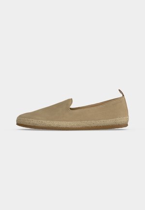 Beige Slip-On-Espadrille mit Wildleder-Obermaterial, geflochtener Jutemittelsohle, Gummilaufsohle und Zuglasche an der Ferse vor einfarbig hellem Hintergrund.