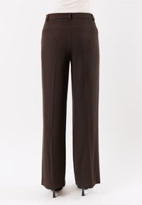 Pantaloni marroni a gamba larga con frontale piatto, passanti per la cintura e una texture di tessuto liscia. I pantaloni presentano un aspetto pulito e sartoriale.