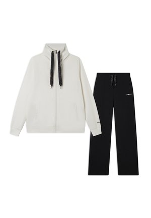 Giacca bianca con zip e colletto alto, abbinata a pantaloni sportivi neri con un piccolo logo e vita regolabile con cordino.
