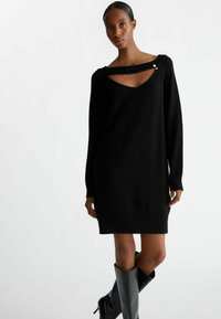 Abito maglione nero con scollatura a V profonda e un design di ritaglio unico. Polsini e orlo a coste, realizzato in un tessuto morbido con una texture liscia.
