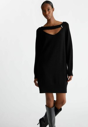 Abito maglione nero con scollatura a V profonda e un design di ritaglio unico. Polsini e orlo a coste, realizzato in un tessuto morbido con una texture liscia.