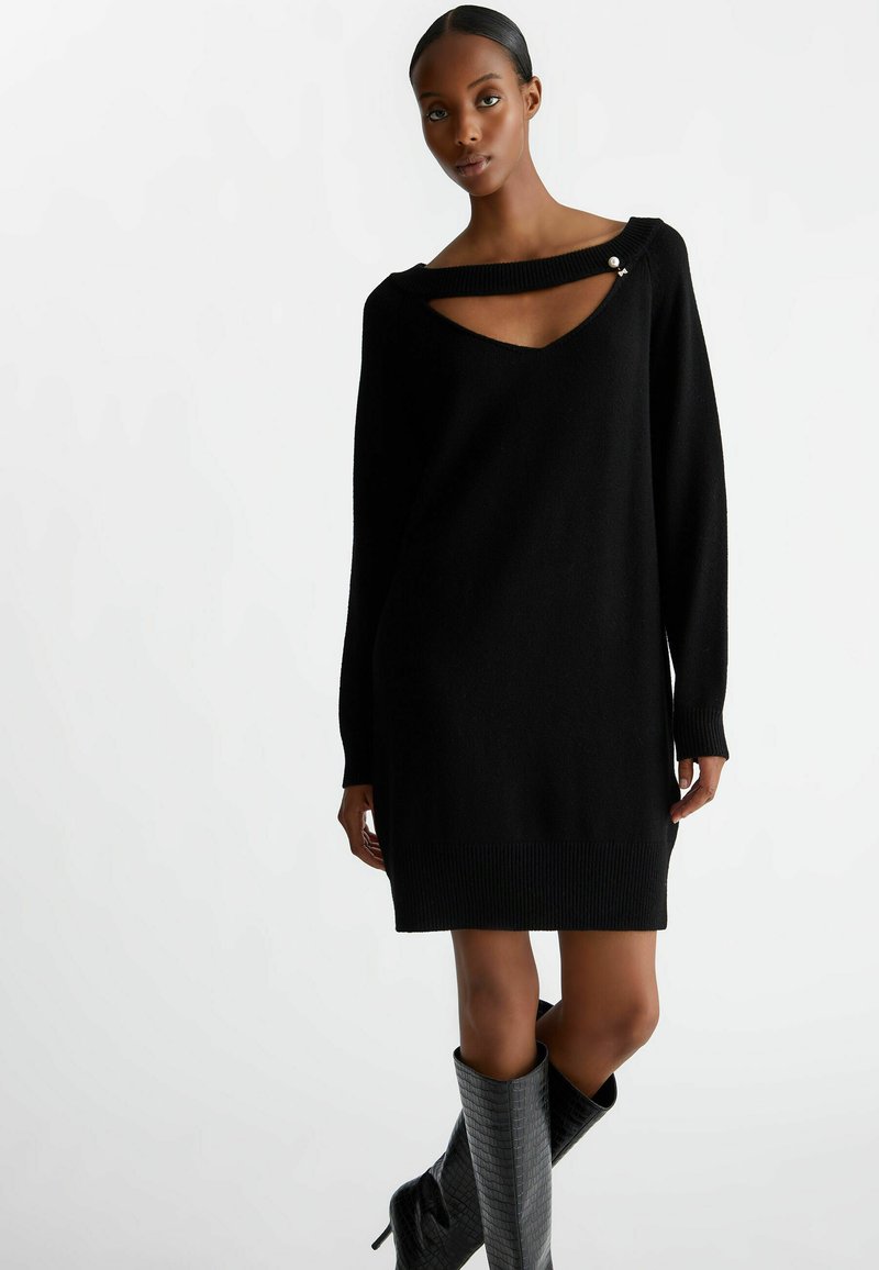 Abito maglione nero con scollatura a V profonda e un design di ritaglio unico. Polsini e orlo a coste, realizzato in un tessuto morbido con una texture liscia.