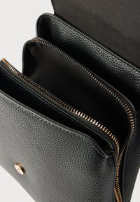 Μαύρο δερμάτινο τσάντα χιαστί με υφή, μεταλλικά στοιχεία σε χρυσό τόνο και τρεις θήκες με φερμουάρ, επενδεδυμένες με απαλό ύφασμα.