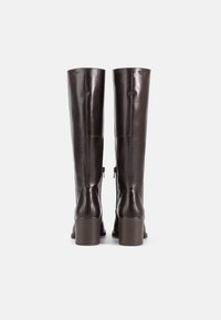 Barna bőr, térdfelett érő csizmák sima felülettel, négyzetes sarkúak és hátsó cipzárral záródnak. Szilárd, jól megtervezett forma.