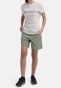 Ljust färgad, kortärmad t-shirt med vågmönster; matchad med olivgröna shorts; bärs med svarta, strukturerade träningsskor.