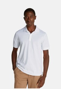 Polo shirt bianca realizzata in cotone morbido, con colletto classico e maniche corte, dal taglio rilassato e senza motivi o dettagli particolari.