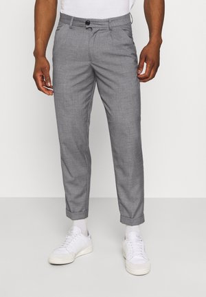 Mann trägt schmale graue Anzughose, am Saum umgeschlagen, kombiniert mit weißen Socken und weißen Sneakern.