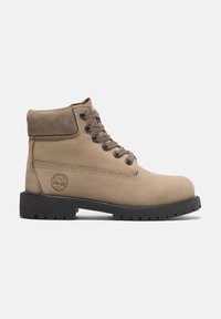 Botas de tobillo de ante beige con un cuello acolchado, suela de goma negra, cordones redondos y un pequeño logo de árbol en el lateral. Detalle de costura reforzada.