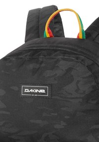 Mochila negra fabricada en tejido texturizado, con un prominente parche de logo y un bucle colgante multicolor en rojo, verde y amarillo.