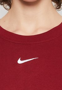 Czerwona bawełniana bluza z ribbowanym dekoltem i białym logo Nike na froncie. Gładka tekstura, casualowy design.
