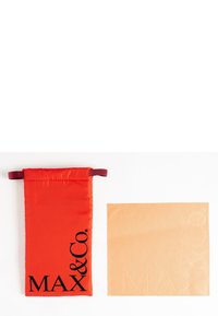 Pungă din material textil roșu cu șnur, cu text logo închis și accente bordô. Alături se află un pătrat neted, de culoare bej, cu detalii de brand embosate.