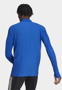 Polo a maniche lunghe di un vivace blu, realizzato in tessuto texturizzato con colletto, caratterizzato da un design aderente e dettagli a contrasto.