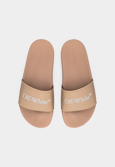 Ζευγάρι μπεζ σανδάλια slip-on με λευκά λογότυπα "Off-White™" στα λουράκια, τοποθετημένα δίπλα δίπλα σε λευκό φόντο.