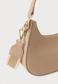Sac à main en forme de croissant beige avec une fermeture éclair et des fermoirs dorés, attaché à une bandoulière en tissu rayé beige et crème.