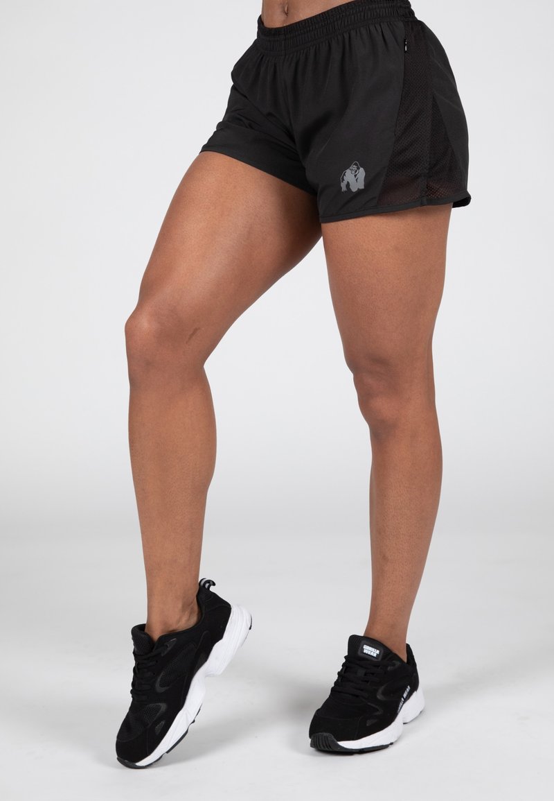 Zwarte sportshorts met een mesh zijpaneel, voorzien van een zilveren gorillalogo. Zwarte sportschoenen met witte zolen maken de look compleet.
