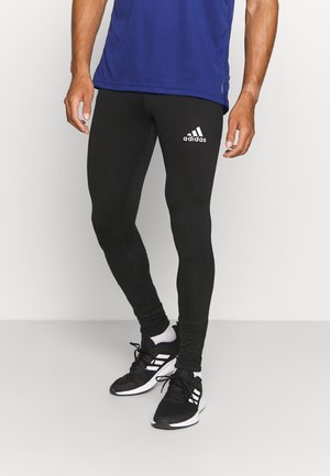 Schwarze Sportleggings mit enganliegendem Design, ausgestattet mit einem auffälligen weißen Adidas-Logo. Glatte Textur, kombiniert mit schwarzen Sportschuhen.