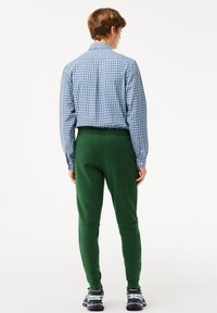 Chemise à carreaux bleus, joggeurs verts, taille élastique et baskets multicolores. Tissu lisse avec une coupe ajustée et des jambes fuselées.