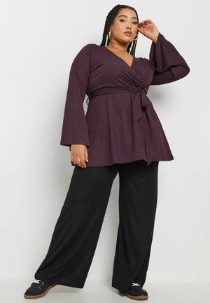 Plum wrap top with bell sleeves, cinched waist detail, paired with black wide-leg pants and black sneakers. Smooth, textured fabric.