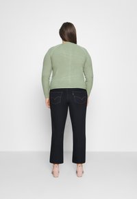 Suéter de canalé verde claro con mangas largas, combinado con pantalones de mezclilla oscuros que presentan costuras en contraste y un corte ajustado.