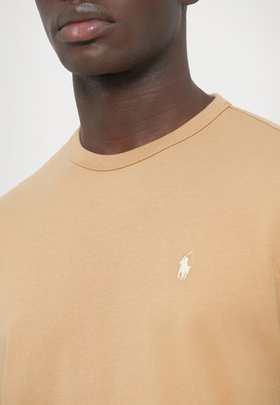 Bézs pamut póló környakú kivitelben, bal mellrészen kis fehér polo logóval és bordázott gallér részlettel.