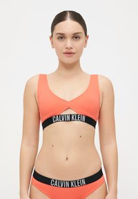 Calvin Klein Bralette in leuchtendem Korallenrot mit breiten Trägern, einem Ausschnitt-Design und einem kontrastierenden schwarzen Elastikband mit Logo.