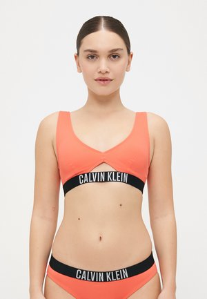 Calvin Klein bralette in bright coral, featuring wide straps, a cutout design, and a contrasting black elastic band with logo.