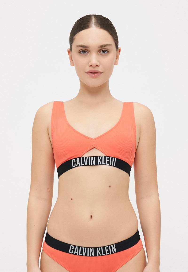 Calvin Klein Bralette in leuchtendem Korallenrot mit breiten Trägern, einem Ausschnitt-Design und einem kontrastierenden schwarzen Elastikband mit Logo.