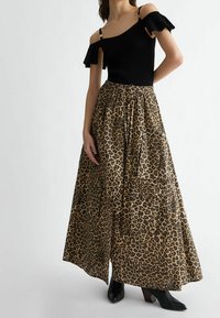 Schwarzes geripptes Top mit schulterfreien Ärmeln kombiniert mit einem Maxirock im Leopardenprint, der über einen elastischen Bund und seitliche Taschen verfügt; schwarze Knöchelboots.