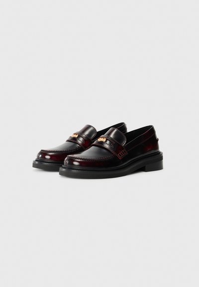 Burgundy läder loafers med en tjock svart sula, som har ett dekorativt band över ovansidan och detaljerad sömnad längs sömmarna.