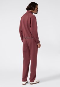 Bordowy dres z wysokim kołnierzem, białymi akcentami w talii, luźnym kroju i miękką teksturą. W zestawie z białymi trampkami slip-on.