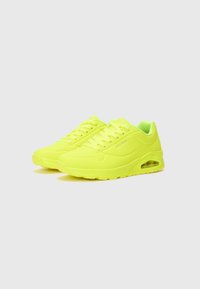 Des chaussures de sport néon jaunes avec des panneaux texturés et une semelle rembourrée. Dispose d'un design à lacets et d'un amorti d'air visible sur le côté.