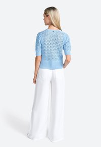 Maglione azzurro chiaro a maglia con maniche corte, caratterizzato da un motivo in pizzo texturizzato, abbinato a pantaloni bianchi a gamba larga. Vista posteriore.