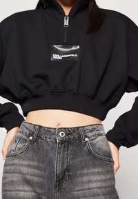 Svart croppad sweatshirt med dragkedja vid halsen och logotypmärke, kombinerad med högmidjade grå jeans med blekt utseende och knäppning.